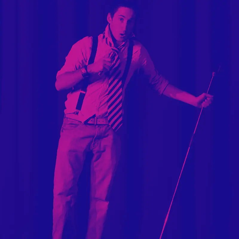 a comic on stage holding a mic stand and tilting it to the side